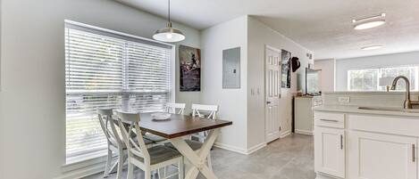 A modern kitchen with white cabinetry, a wooden dining table, and a large window with blinds.