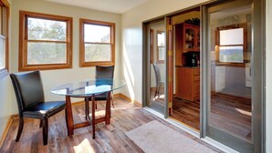 A dining area with a glass table and chairs, wooden flooring, and large windows.
