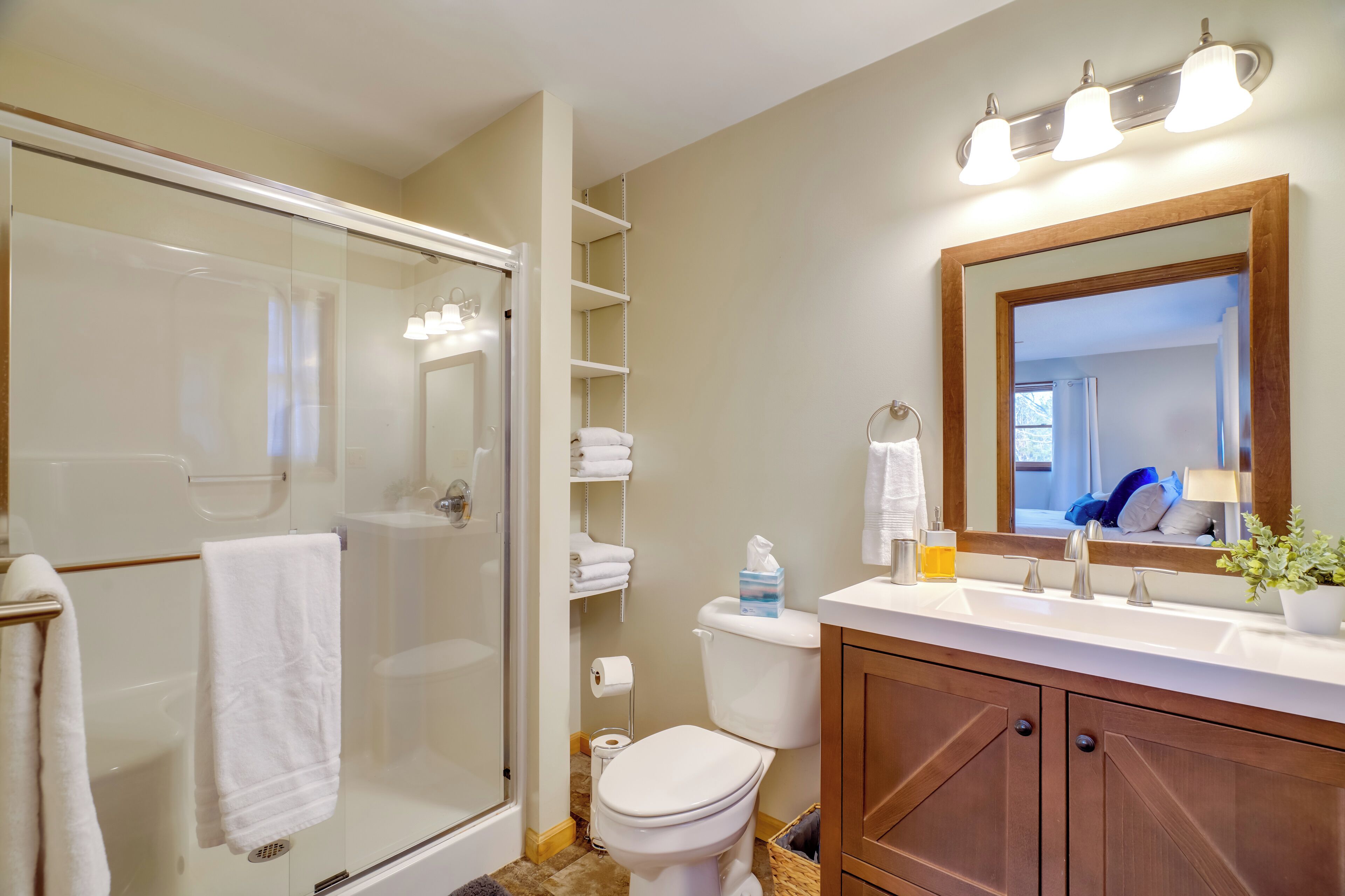 A modern bathroom with a glass-enclosed shower, a toilet, a sink with a mirror, and shelves with towels.
