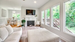 A spacious living room with a fireplace, large windows, and a view of the outdoors. - Bright & Elegant Home in High Point w/ Deck! (High Point)
