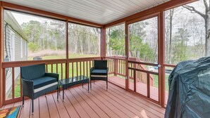 A covered porch with two wicker chairs and a small table, overlooking a grassy yard and trees. - Toano Home w/ Screened Porch: Steps to Lake! (Toano)