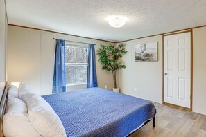 A bedroom with a bed, curtains, a potted plant, and a door. - Pet-friendly Home ~ 5 Mi to Blue Ridge Parkway! (Asheville)