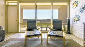 Ein Zimmer mit zwei Sesseln, die eine große Glasschiebetür zu einer Terrasse mit Blick auf eine Brücke und eine Rasenfläche zeigen.
