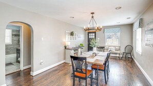 A spacious dining area with a wooden table and chairs, a chandelier, and a view of the kitchen.