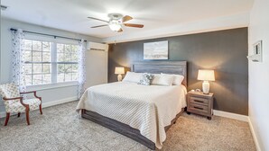 A bedroom with a bed, a chair, a nightstand, a ceiling fan, and a window with curtains.