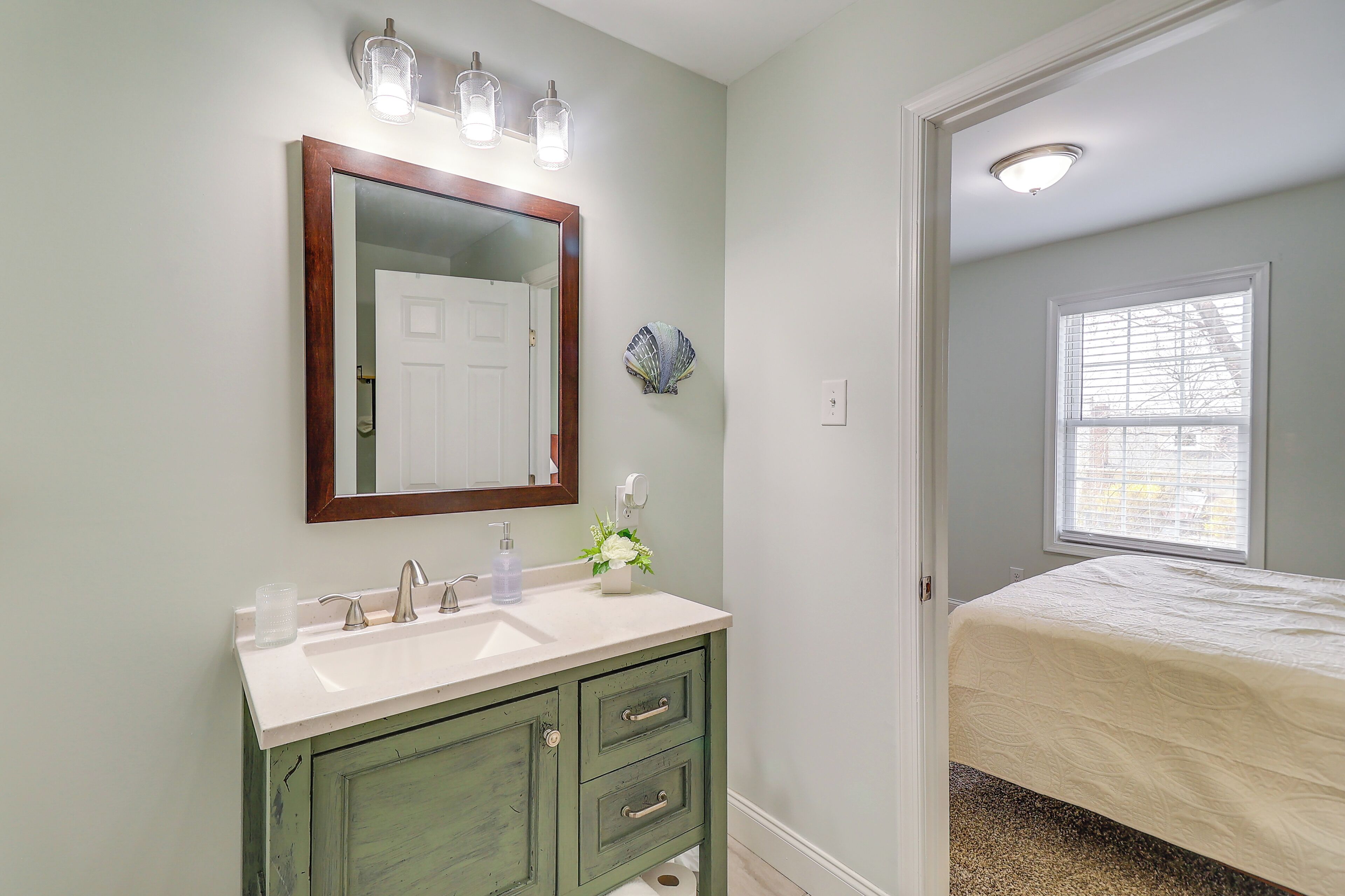 A bathroom with a white sink, green vanity, and a mirror with three lights.