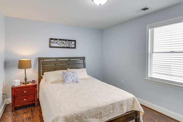 A bedroom with a bed, nightstand, lamp, and a window with blinds.