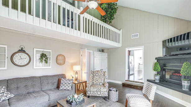 A spacious living area with a grey sofa, a patterned armchair, a wooden coffee table, and a fireplace.