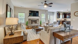 A spacious living room with a fireplace, a ceiling fan, and a kitchen in the background. - Spacious Aiken Home ~ 8 Mi to Downtown! (Aiken)