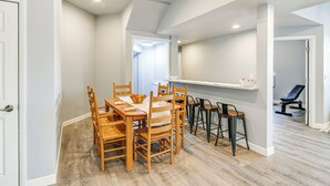 Ein Essbereich mit Holztisch und Stühlen, eine Küchenzeile mit Barhocker und ein Gang zu einem weiteren Zimmer.