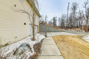 Una propiedad residencial con una escalera de piedra que lleva a una terraza de madera, un camino de hormigón y suelo cubierto de nieve.