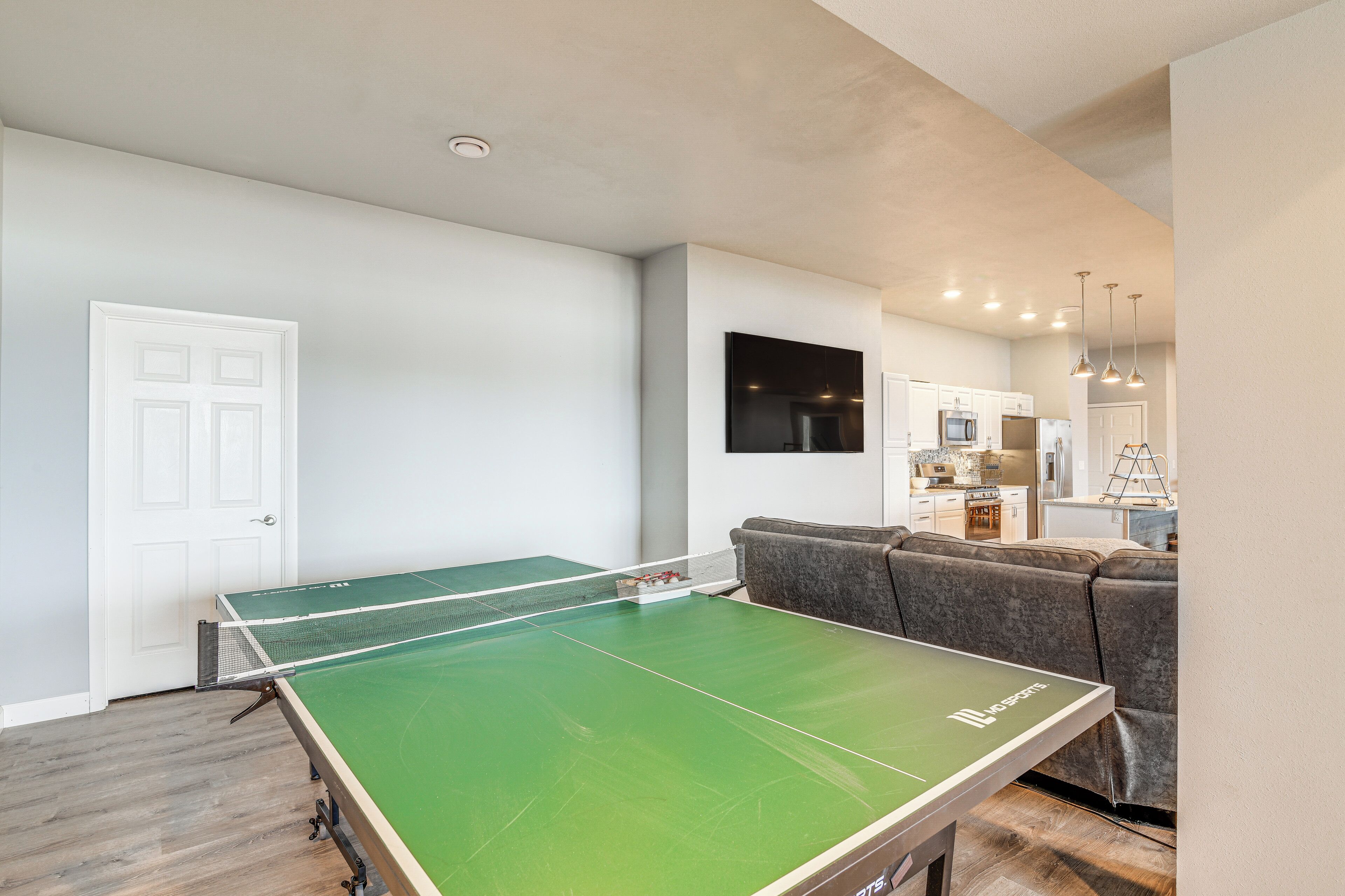 Una mesa de ping pong en una habitación con kitchenette y un sofá gris.
