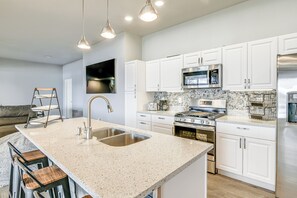A modern kitchen with white cabinets, a granite countertop, stainless steel appliances, and a bar stool area. - Palmer Apartment w/ Peaceful Pond & Kayaks! (Palmer)