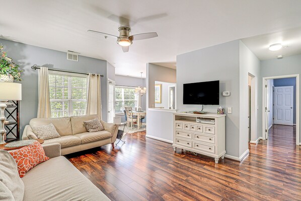 A living room with a sofa, TV, and wooden flooring. - Community Pool & Private Balcony: Chic Lewes Gem (Rehoboth Beach)