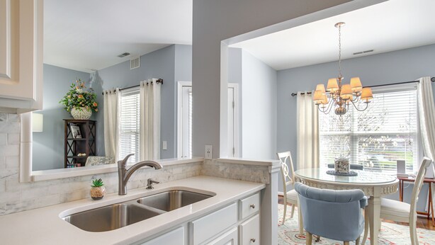 A kitchen with a double sink, white cabinetry, and a dining area with a round table and chairs. - Community Pool & Private Balcony: Chic Lewes Gem (Rehoboth Beach)