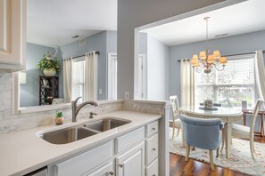 A kitchen with a double sink, white cabinetry, and a dining area with a round table and chairs. - Community Pool & Private Balcony: Chic Lewes Gem (Rehoboth Beach)