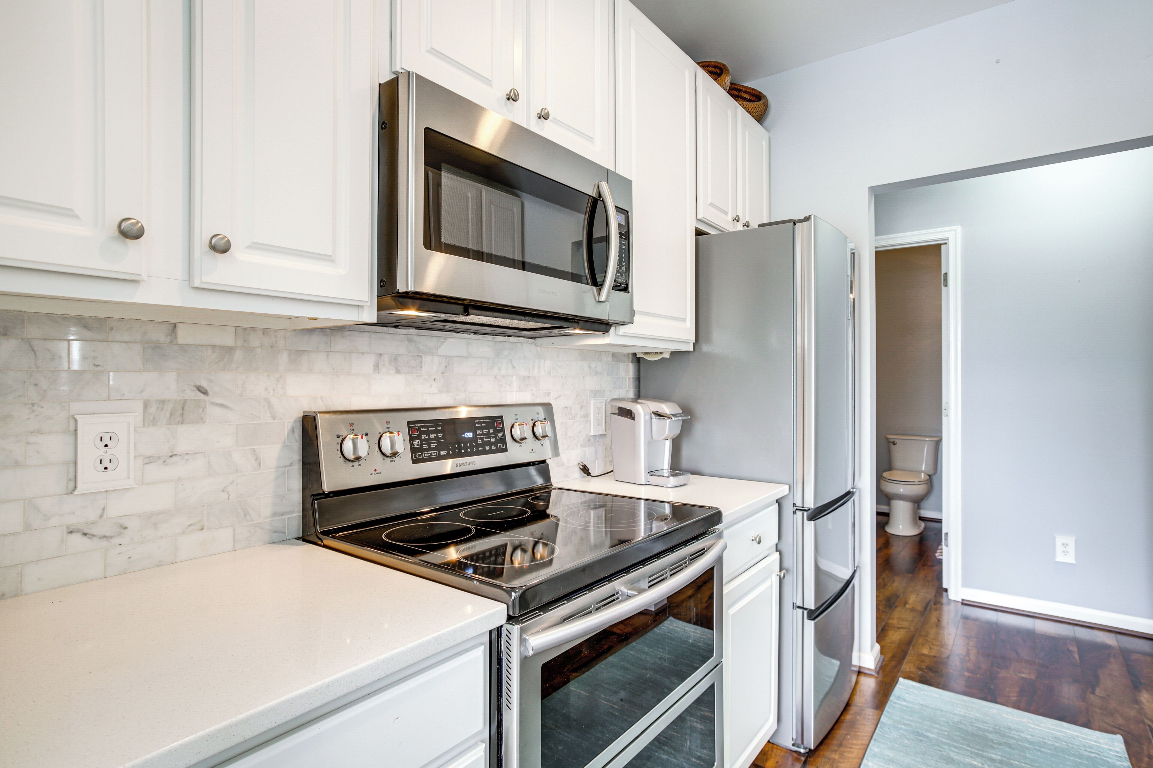 A kitchen with white cabinets, a stainless steel microwave, a built-in oven, and a refrigerator.