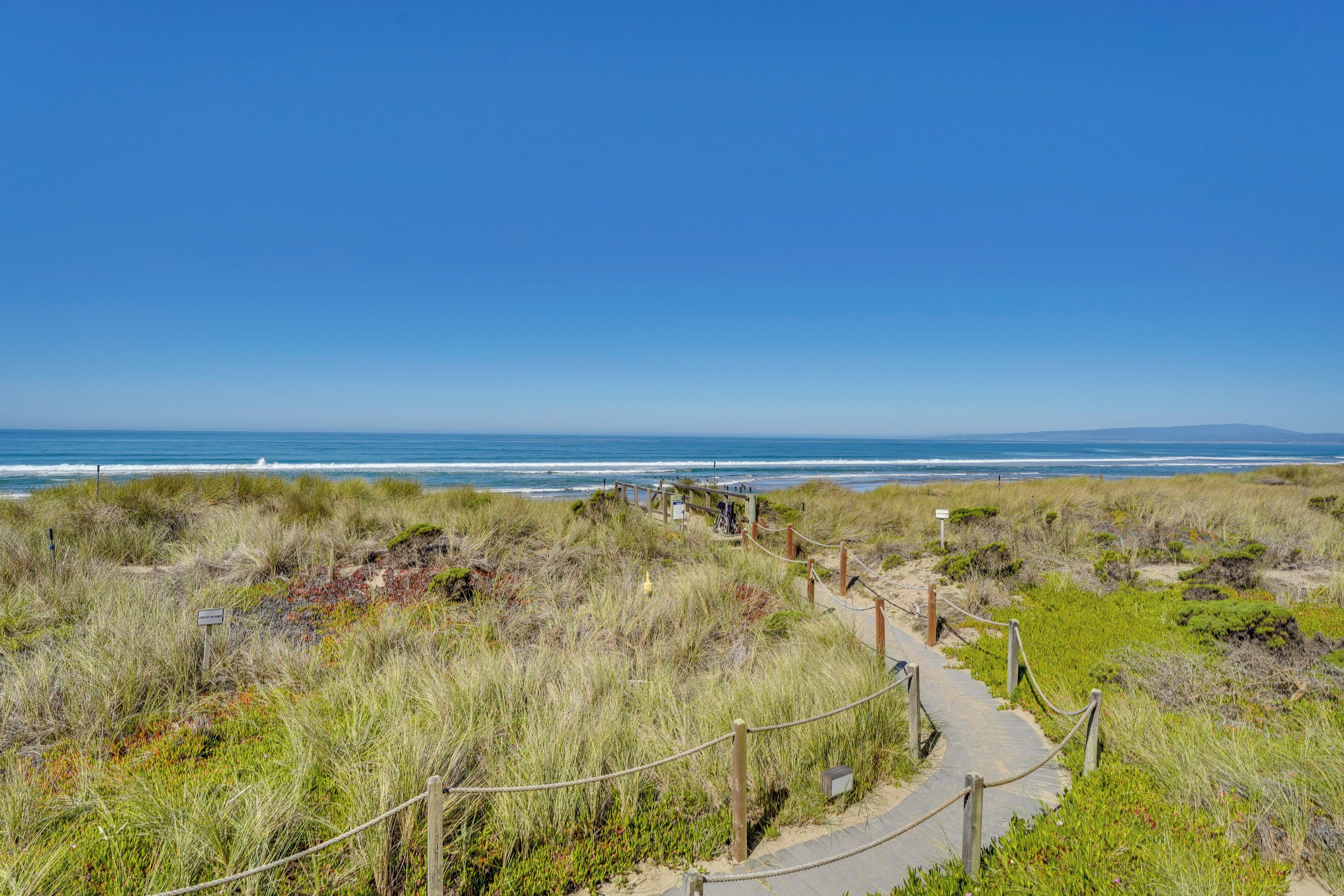 A coastal pathway with wooden railings, leading to a beach with ocean views.