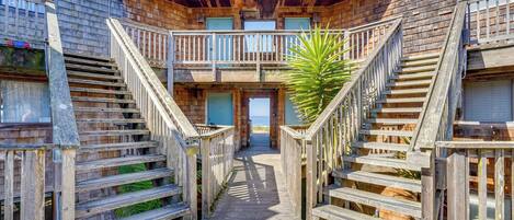A wooden boardwalk leading to a building with multiple balconies and a view of the ocean.