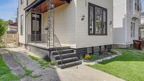 A two-story house with a front porch, a set of stone steps leading to the door, and a small garden area with flowers and shrubs. - Pet-friendly Kentucky Home w/ Deck & Private Yard! (Covington)