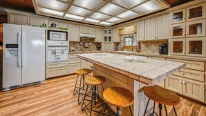 A spacious kitchen with a large island, wooden stools, and a refrigerator. - Broken Bow Cabin w/ Hot Tub & Fishing On-site! (Broken Bow)