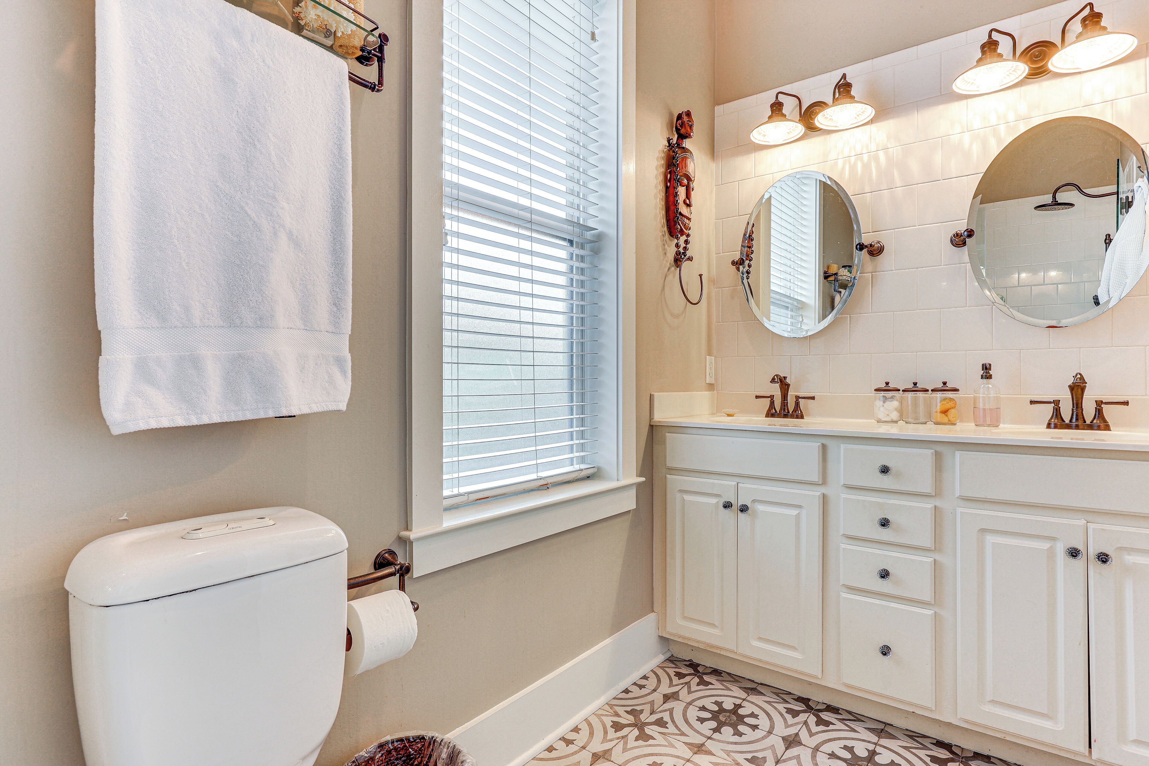 A bathroom with a toilet, a window with blinds, a sink with a mirror, and a vanity with drawers.