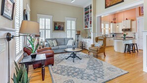 A spacious living room with a sofa, coffee table, and a rug. There is a kitchen area with a dining table and chairs. - Charming Wilmington Cottage - Walk to Downtown! (Wilmington)
