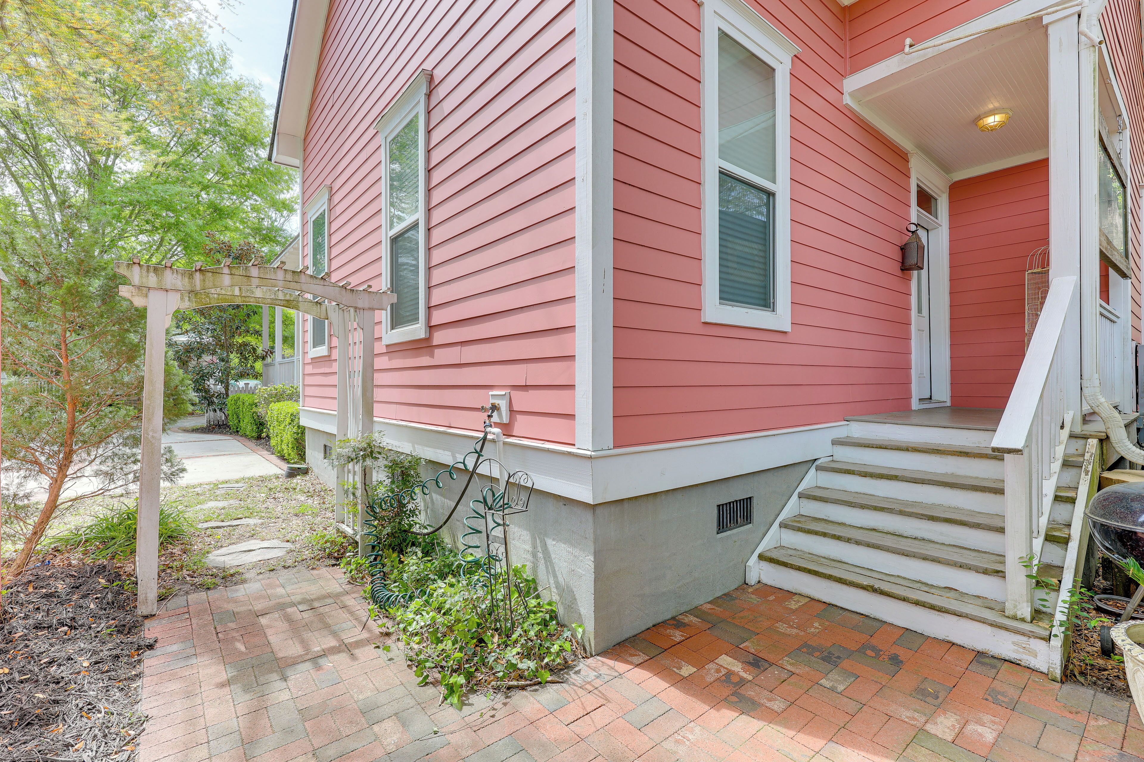 A pink house with a covered porch, a brick pathway, and a small garden area.