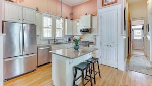 A kitchen with white cabinets, stainless steel appliances, a granite countertop island, and wooden stools. - Charming Wilmington Cottage - Walk to Downtown! (Wilmington)