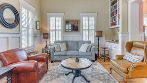 A living room with a sofa, armchair, coffee table, and a bookshelf. - Charming Wilmington Cottage - Walk to Downtown! (Wilmington)