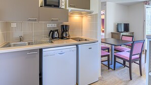 A compact kitchen with a microwave, coffee maker, and dishwasher. There is a dining area with a table and chairs. - Les Rives de Pont Aven - Vacancéole (Pont-Aven)