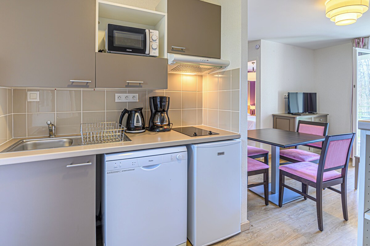 A compact kitchen with a microwave, coffee maker, and dishwasher. There is a dining area with a table and chairs.