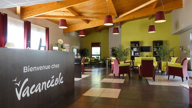 A reception area with a wooden ceiling, a check-in counter, and a seating area with chairs and tables. - Les Rives de Pont Aven - Vacancéole (Pont-Aven)