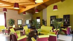A lobby with yellow sofas, red and yellow chairs, wooden ceiling beams, and potted plants. - Les Rives de Pont Aven - Vacancéole (Pont-Aven)