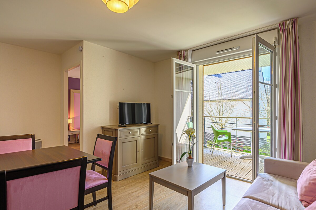 A living room with a sofa, a dining table, chairs, a TV on a cabinet, and a sliding glass door to the outside.