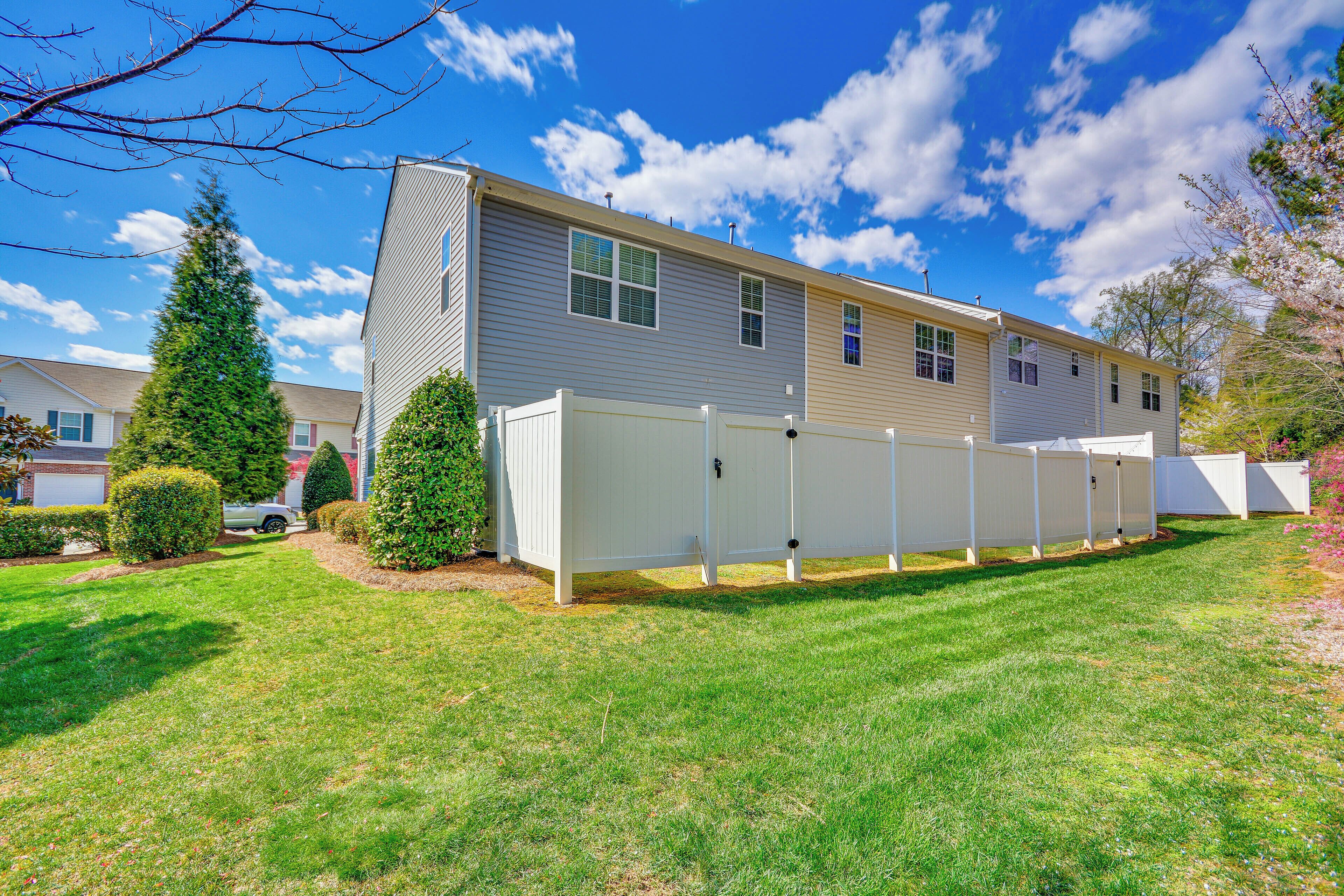 A single-story mobile home with a fenced backyard, a well-maintained lawn, and a clear blue sky.