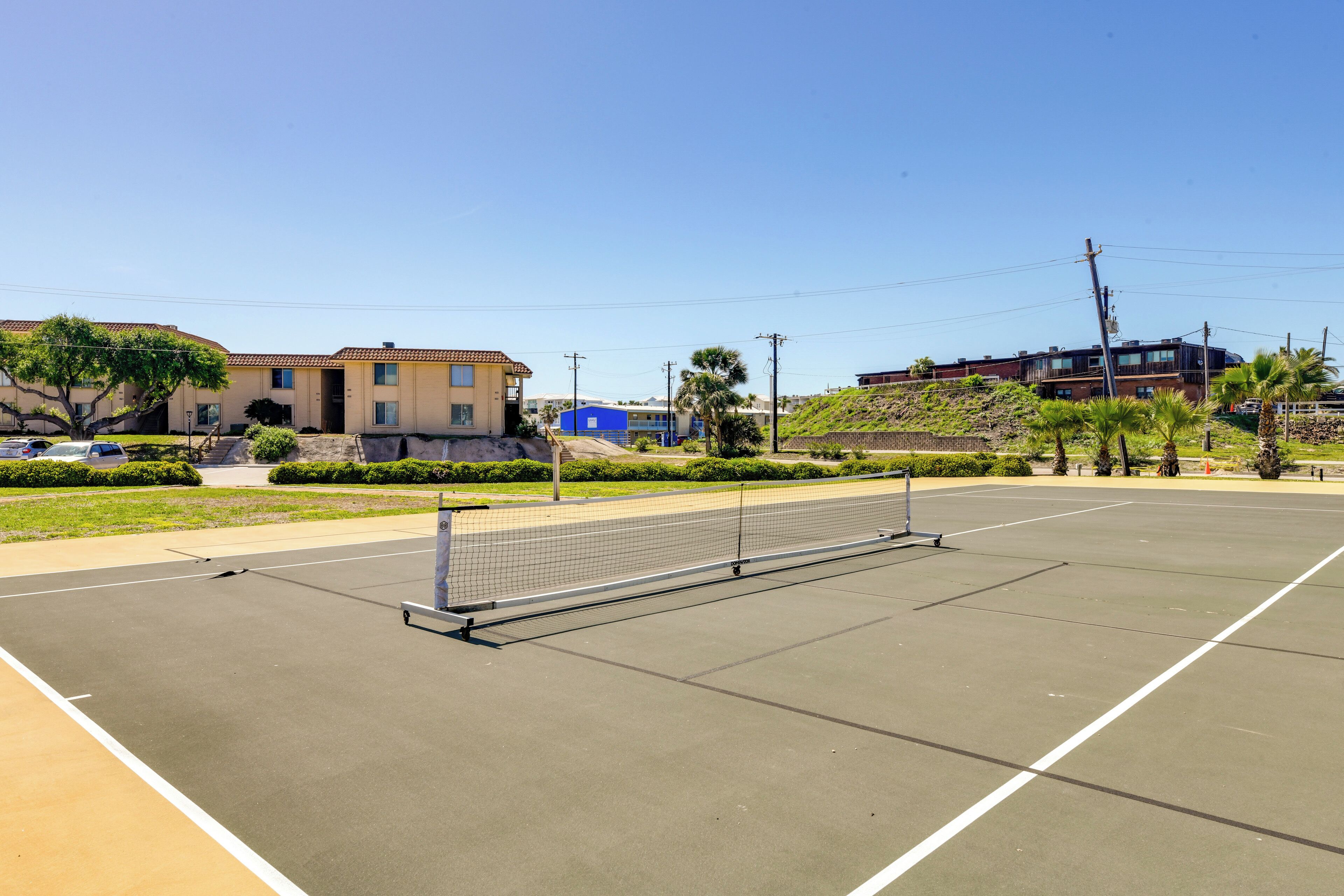 A tennis court with a net, surrounded by buildings and greenery.
