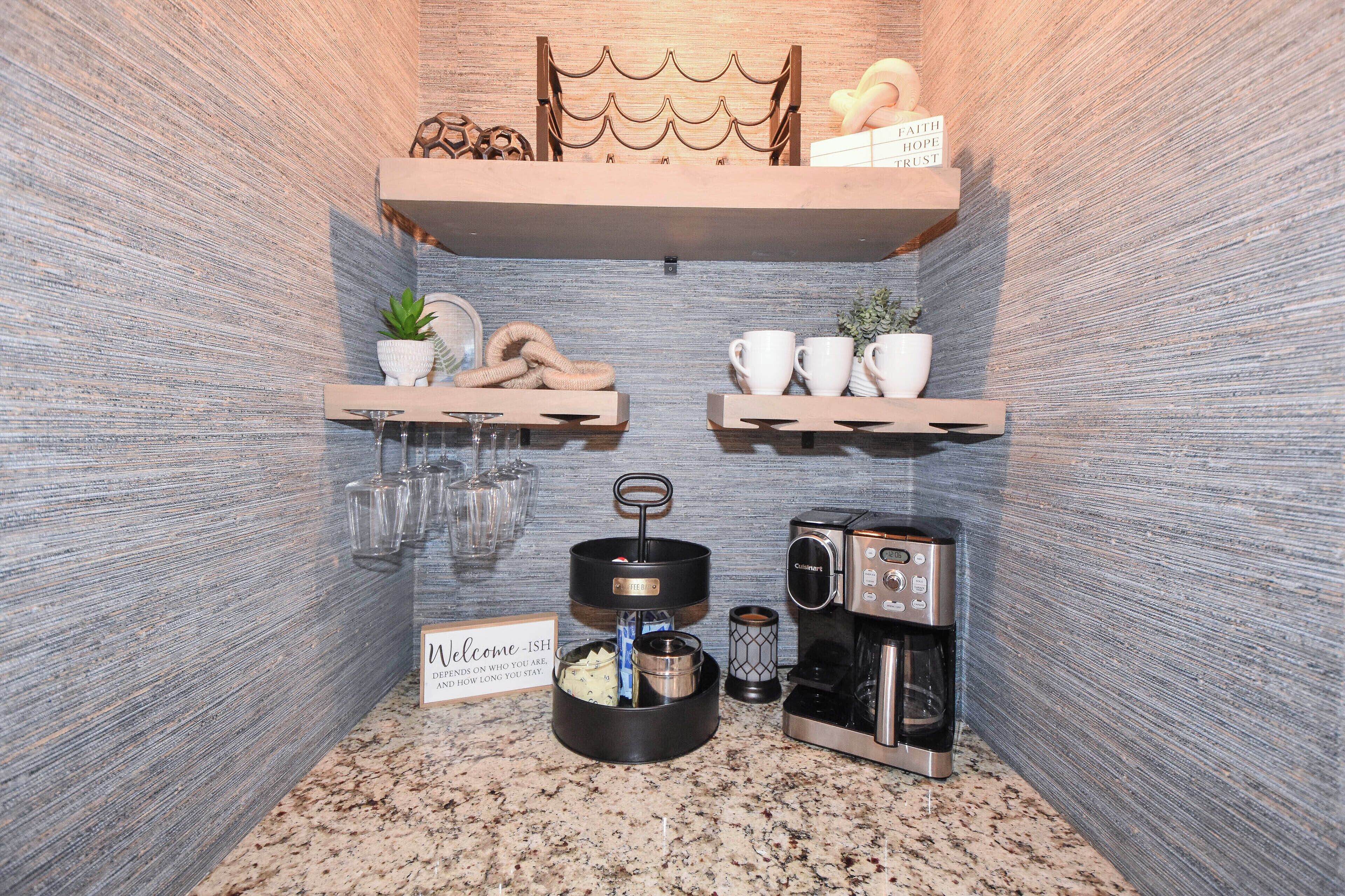 Cocina compacta con cafetera, hervidor de agua y un cartel de bienvenida.