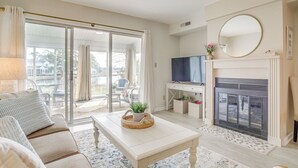 A living room with a sofa, coffee table, TV, fireplace, and a sliding glass door leading to a balcony. - Porch & Water Views: Getaway in Mallard Lakes (Selbyville)