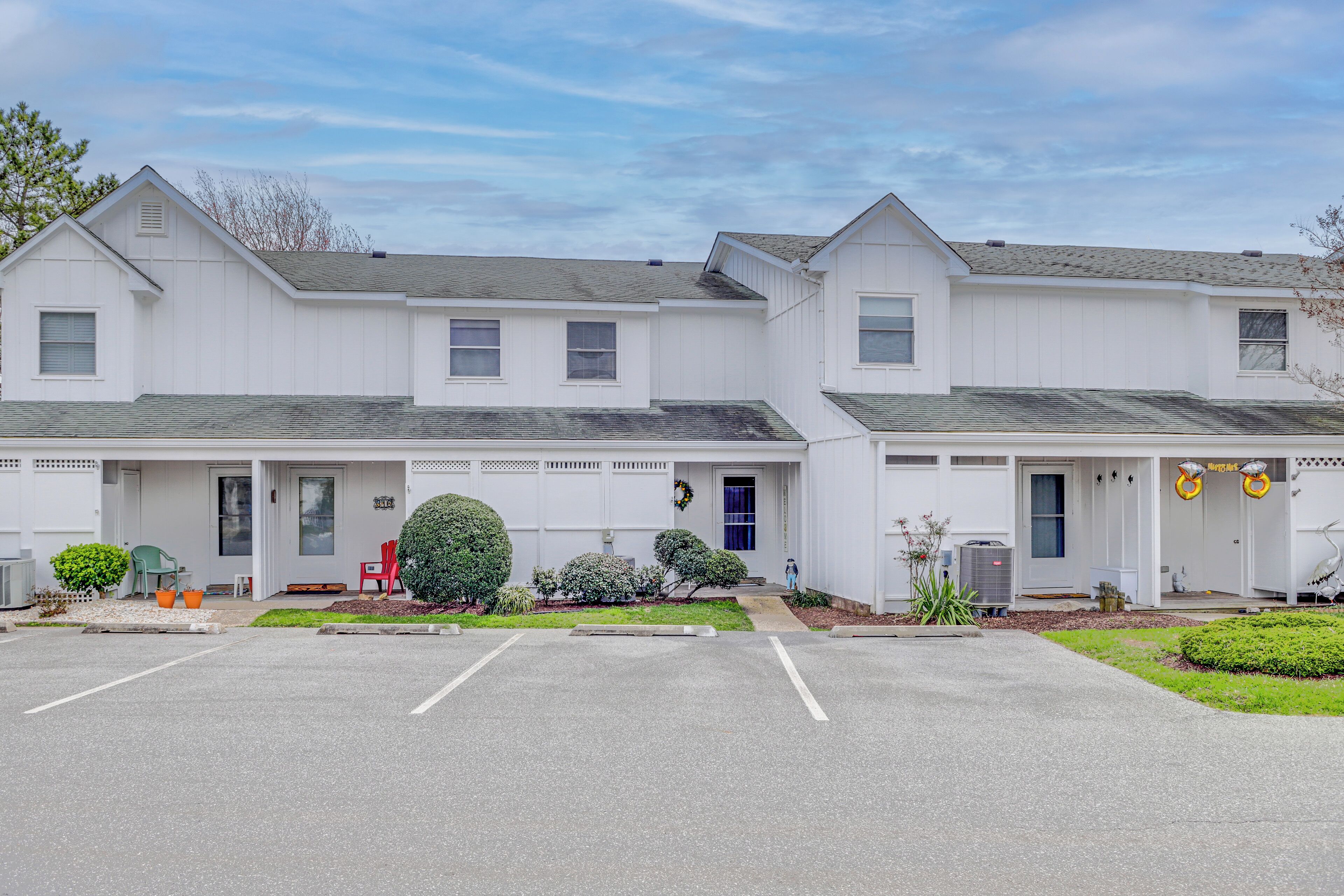 A two-story white building with a front porch, a parking lot, and small landscaping.