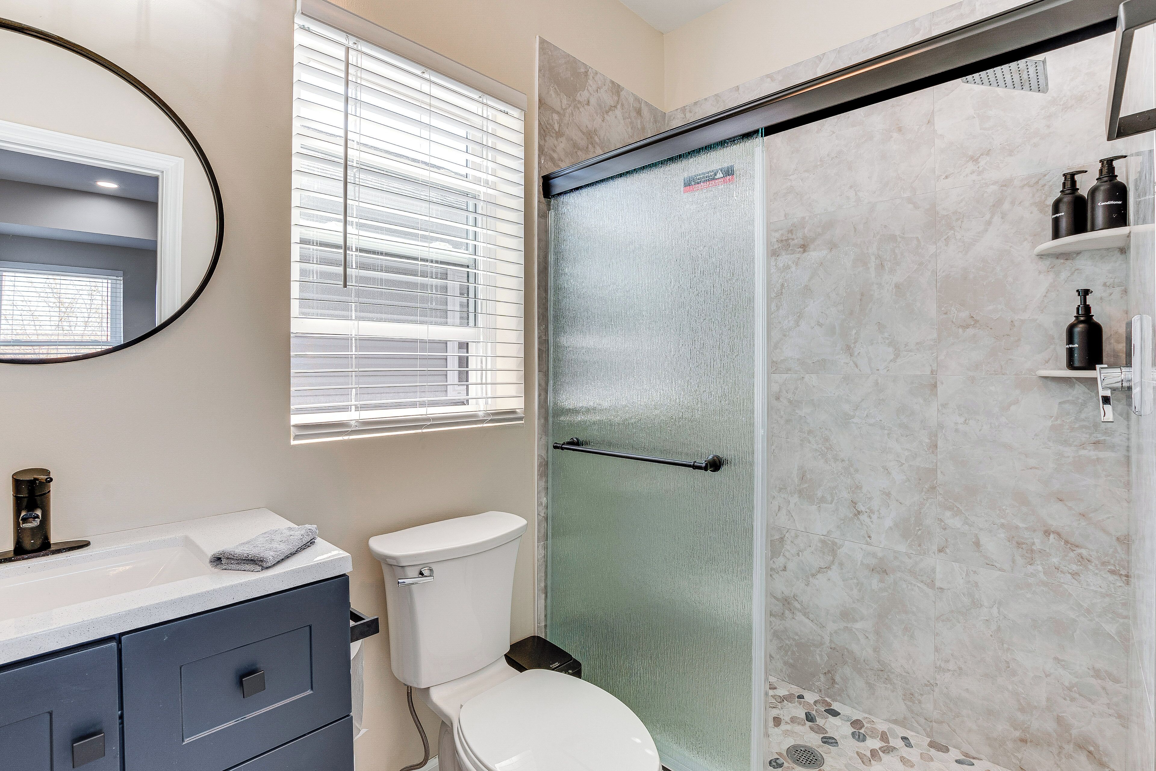 Un baño con inodoro, lavabo con toalla, ducha con puerta de cristal y espejo.