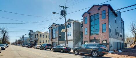 A street lined with multi-story buildings, parked cars, and overhead power lines.