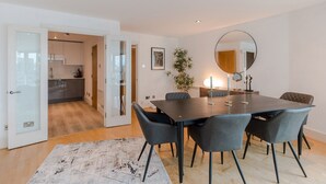 Un espace repas moderne avec une table en bois foncé et six chaises, un grand miroir au mur et une plante en pot.