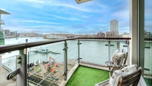 Un balcon avec vue sur une rivière, du matériel de construction et, au loin, un paysage urbain.