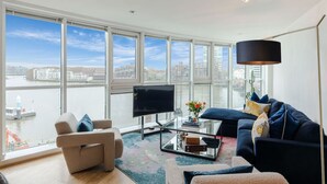 Un salon moderne doté d’une grande fenêtre donnant sur un paysage urbain et sur l’eau.