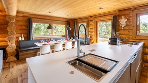 Ein Holzhütten-Interieur mit Küchenbereich, Esstisch und Sitzgelegenheiten.