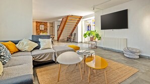 A modern living room with a grey sectional sofa, a wooden staircase, a flat-screen TV, and a small round table. - Maison Rioma - Grande maison à 200m de la plage (Plounéour-Trez)