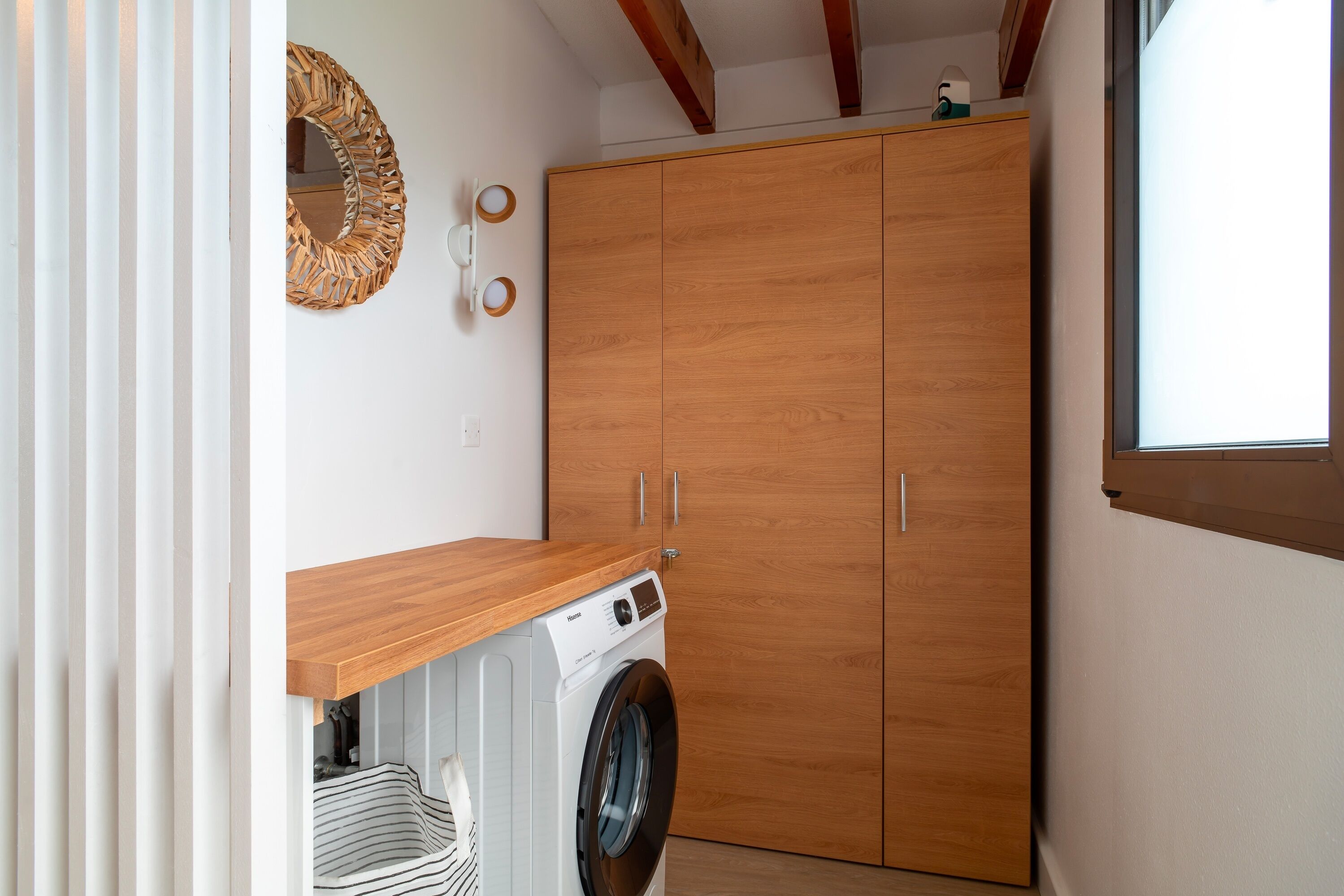 A laundry room with a washing machine, wooden cabinets, and a window.