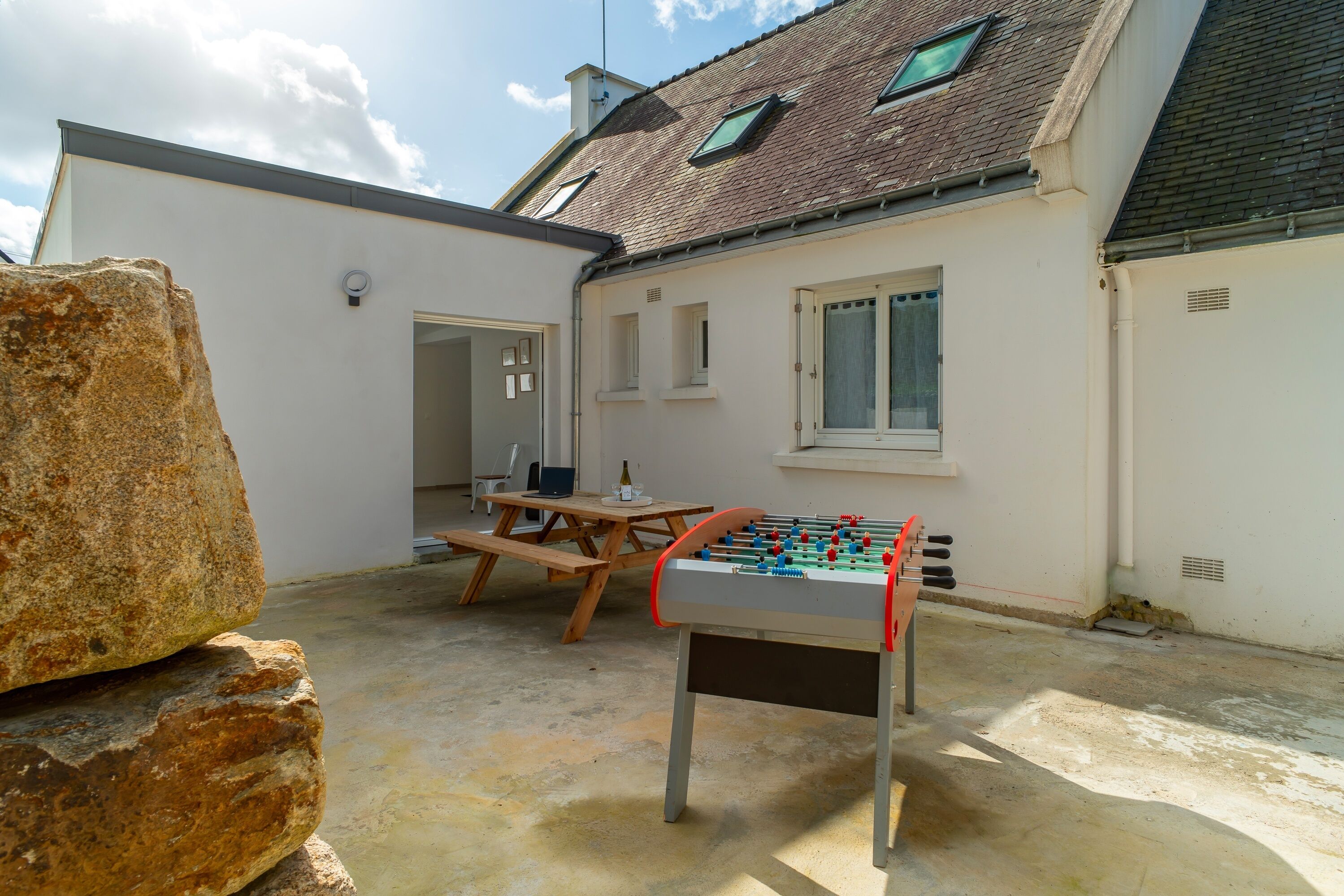 An outdoor patio area with a foosball table, a stone, and a wooden table with chairs.