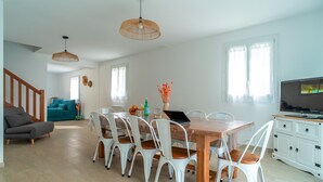 A spacious living area with a dining table, white chairs, a sofa, and a TV. - Villa Ti Vakansou - Avec piscine privée (Clohars-Carnoët)